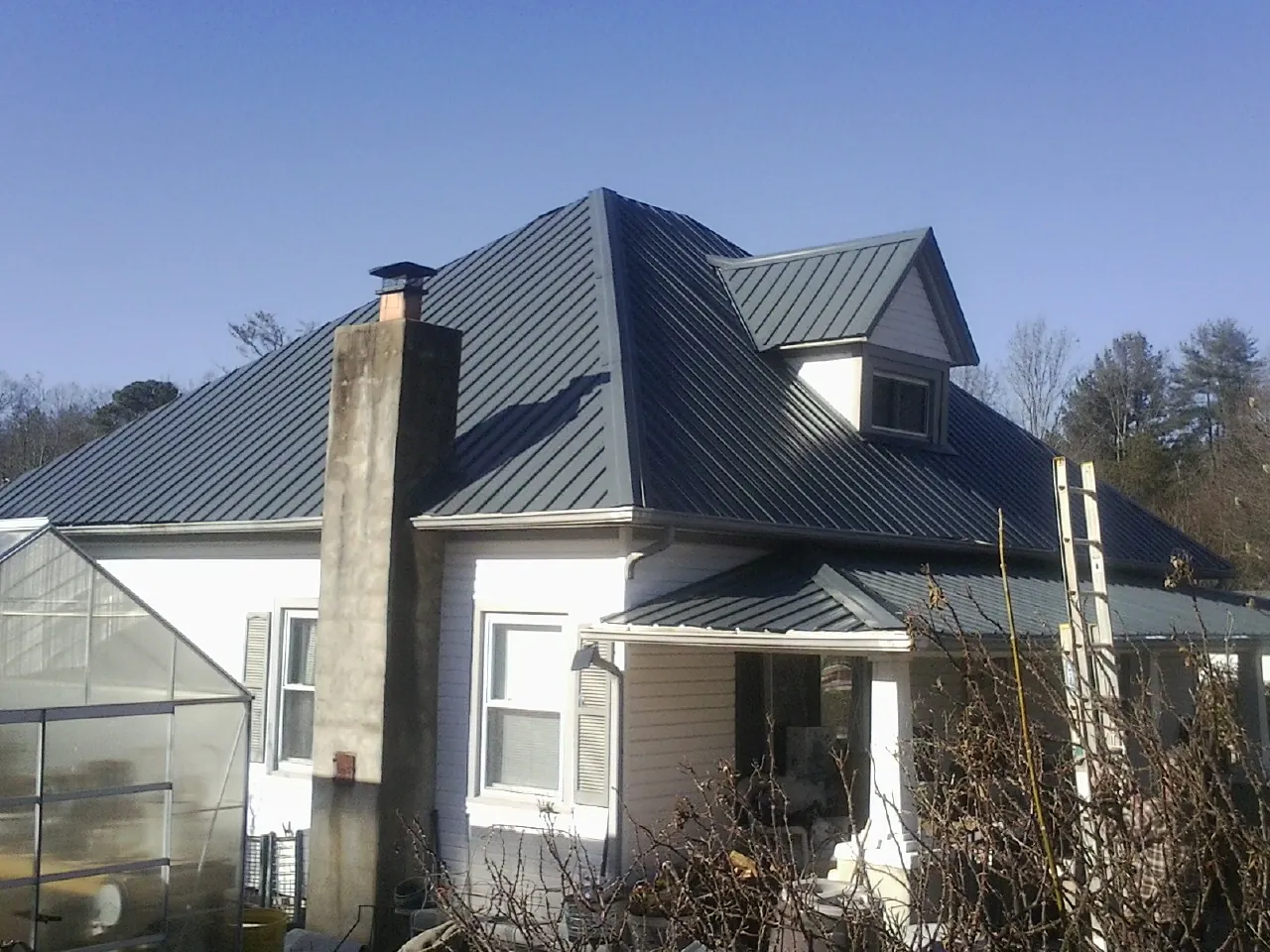 Dark blue standing seam metal roof on a white farmhouse with dormer — Slate & Tile Roof Repair by Roofing Brothers in Cowan