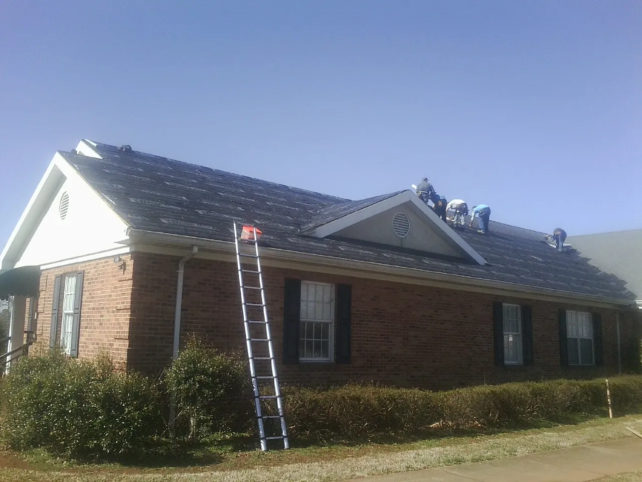 Crew tearing shingles off a brick ranch roof with a ladder set — Emergency Roof Repair work by our crew in Cowan