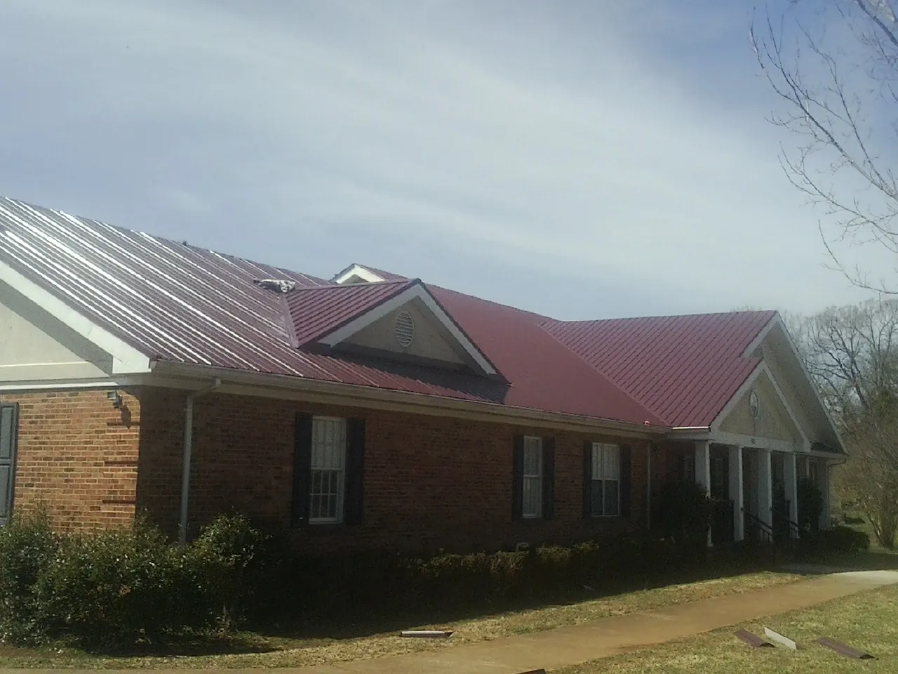 Red metal roof with gabled entries on a long brick building, from a Hail Damage Roof Repair job in Cowan