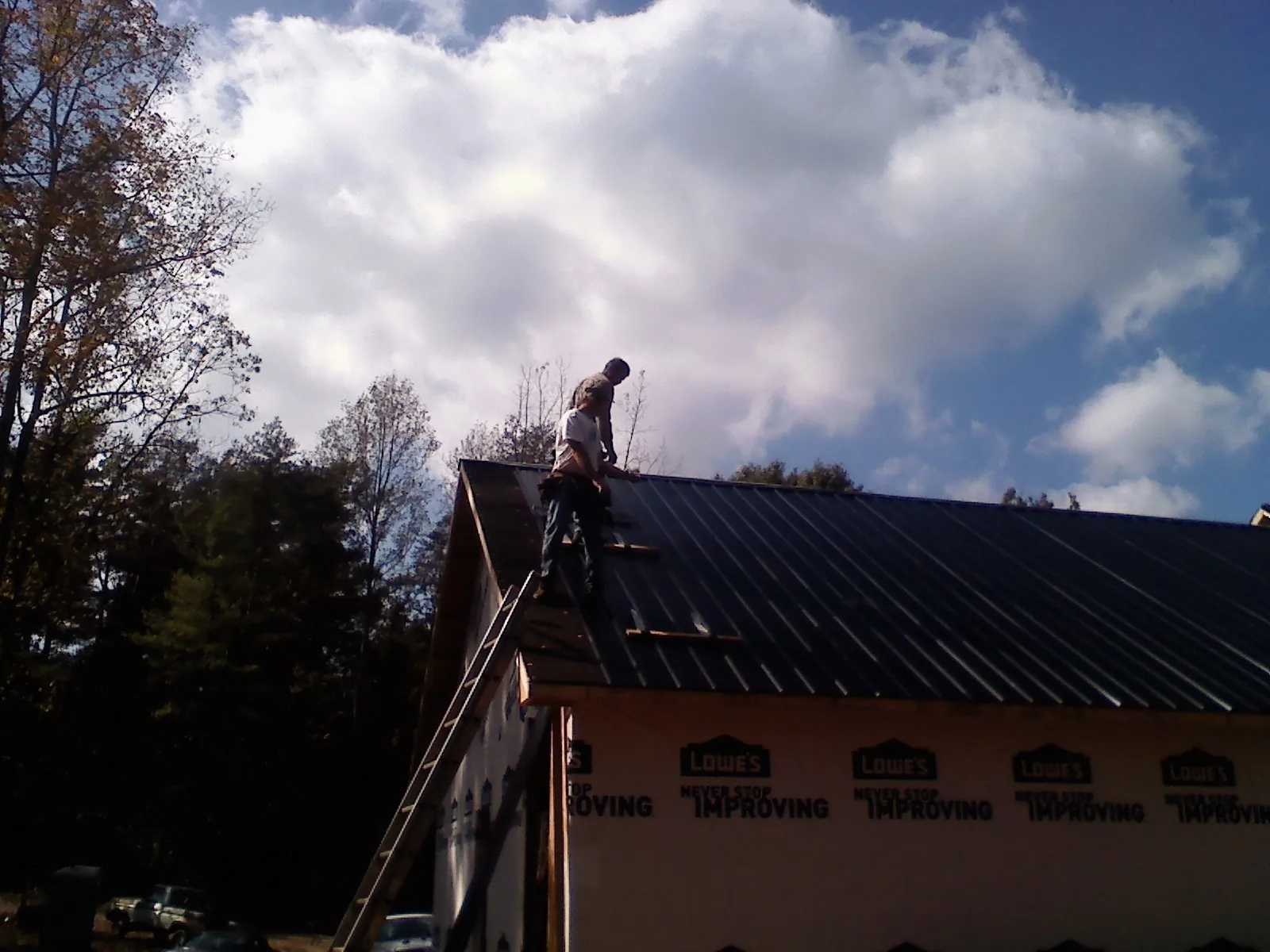 Roofer fastening dark metal panels high against a cloudy sky, from a Roof Inspection job in Cowan