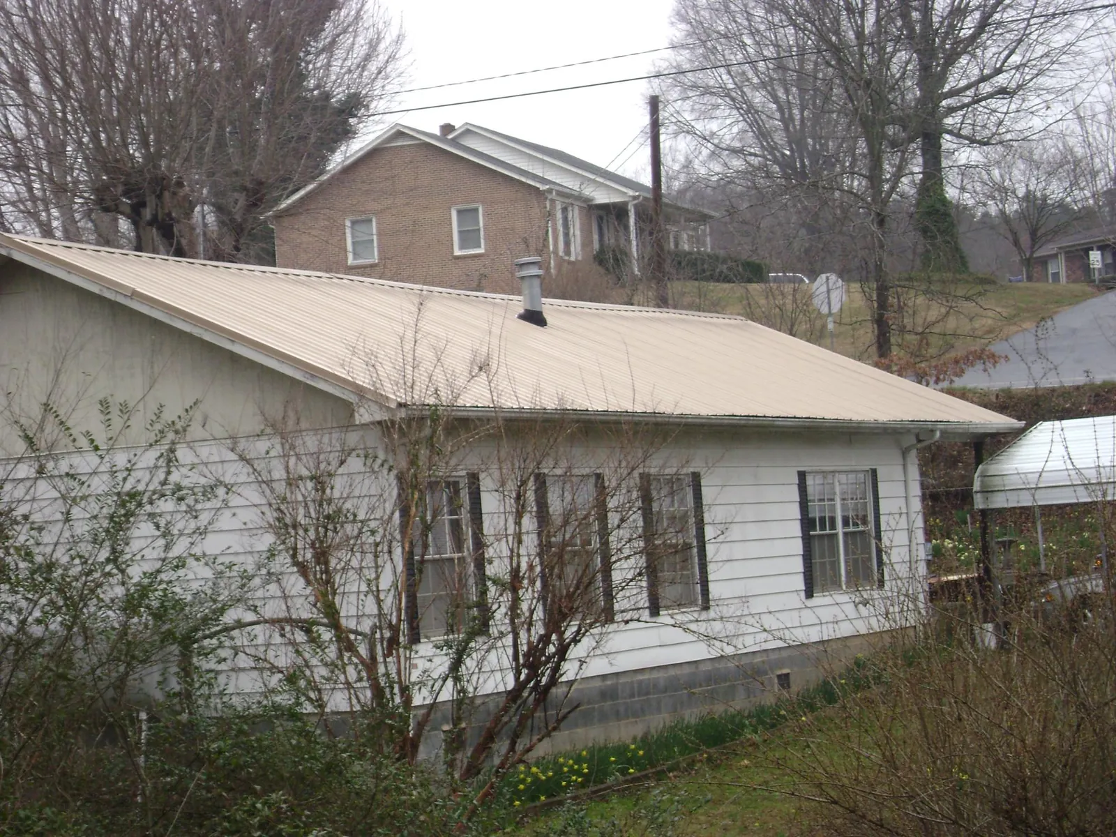 Tan metal roof on a white sided house set into a hillside — Commercial Roofing by Roofing Brothers in Cowan