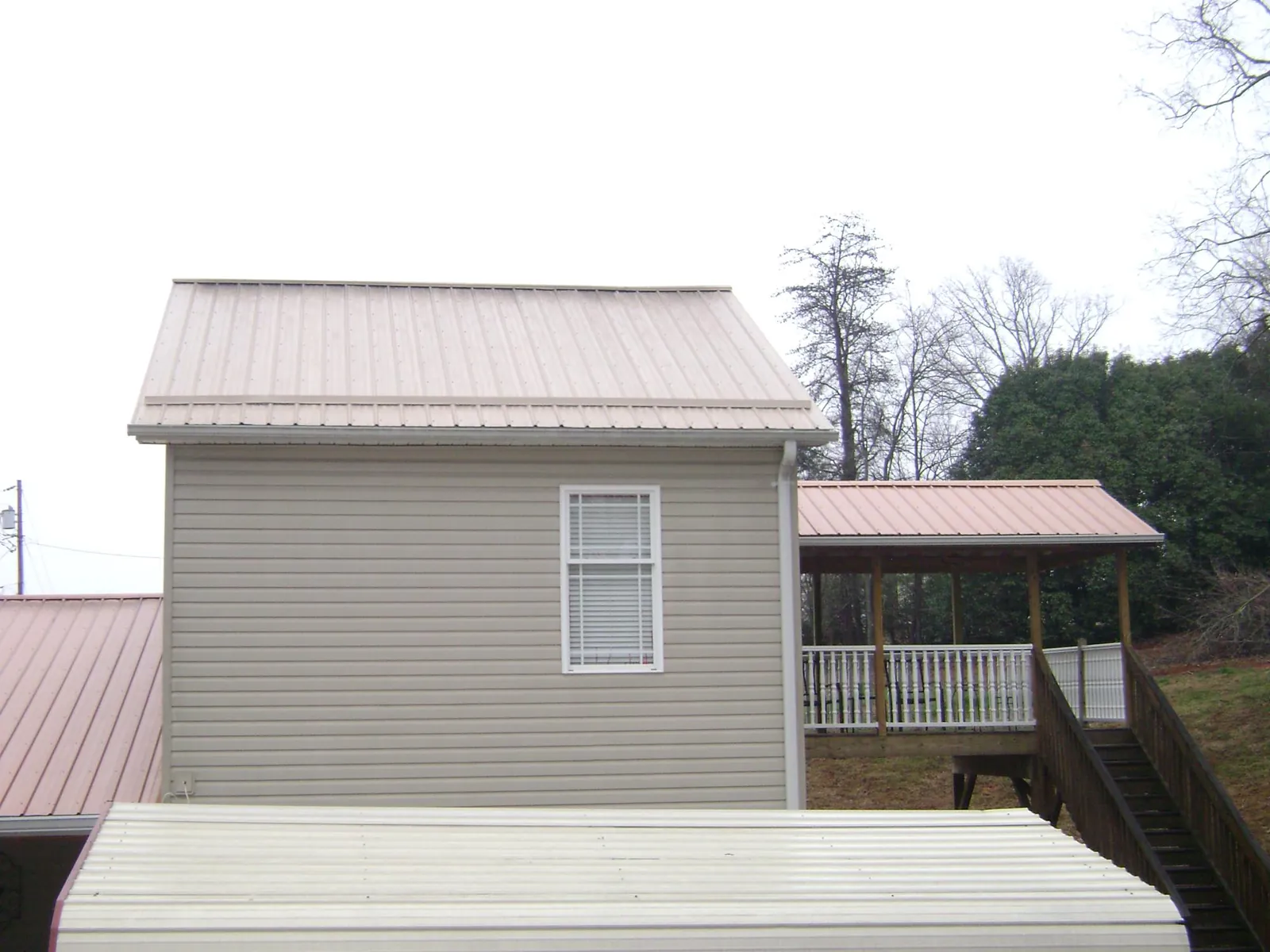 Tan metal roofs on a two story addition and attached porch, from a Roof Replacement job in Cowan